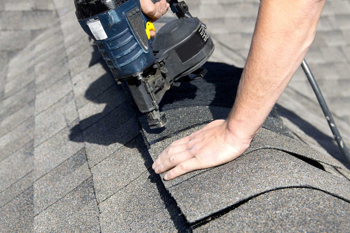 A roofer nails shingles over ridge vent material used on the peak of new residential house construction
