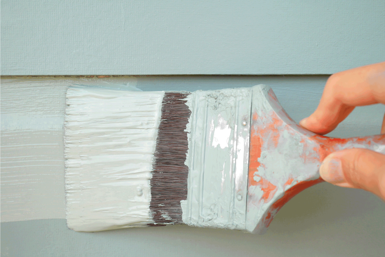 Hand holding brush painting timber wall