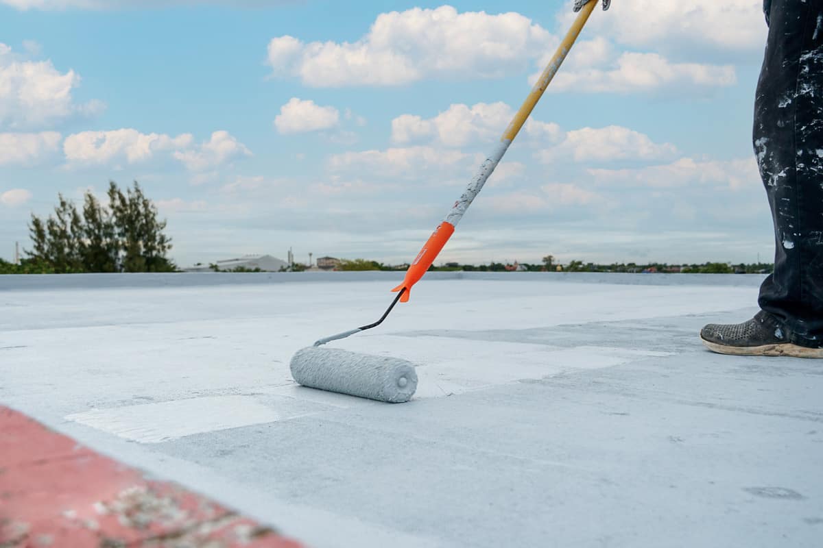 Painting the roofing using a paint roller with white paint