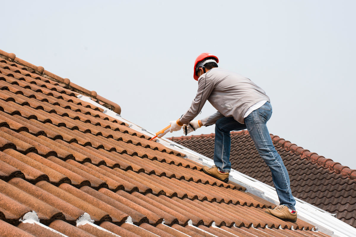 Technician applying caulk on the clay tile roofing