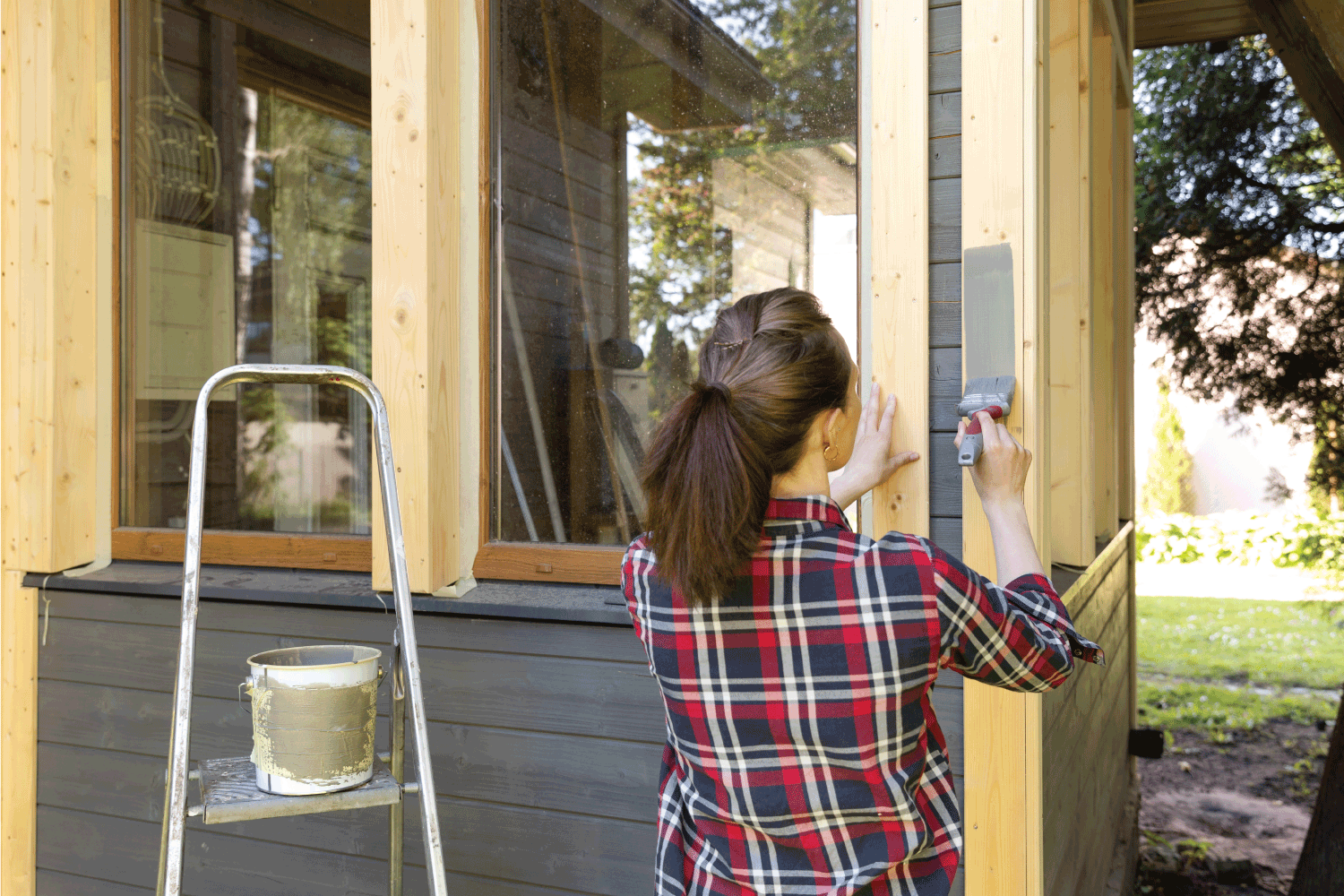 Woman worker painting wooden house exterior wall with paintbrush and wood protective color 