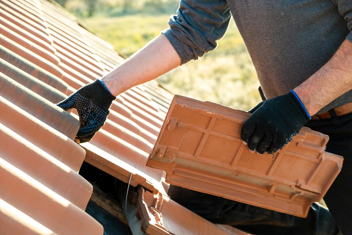Worker hands installing yellow ceramic roofing tiles mounted on wooden boards