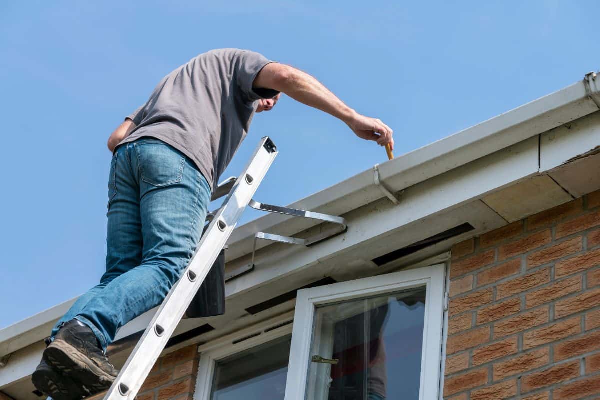 Senior man cleaning gutters on a suburban English house.