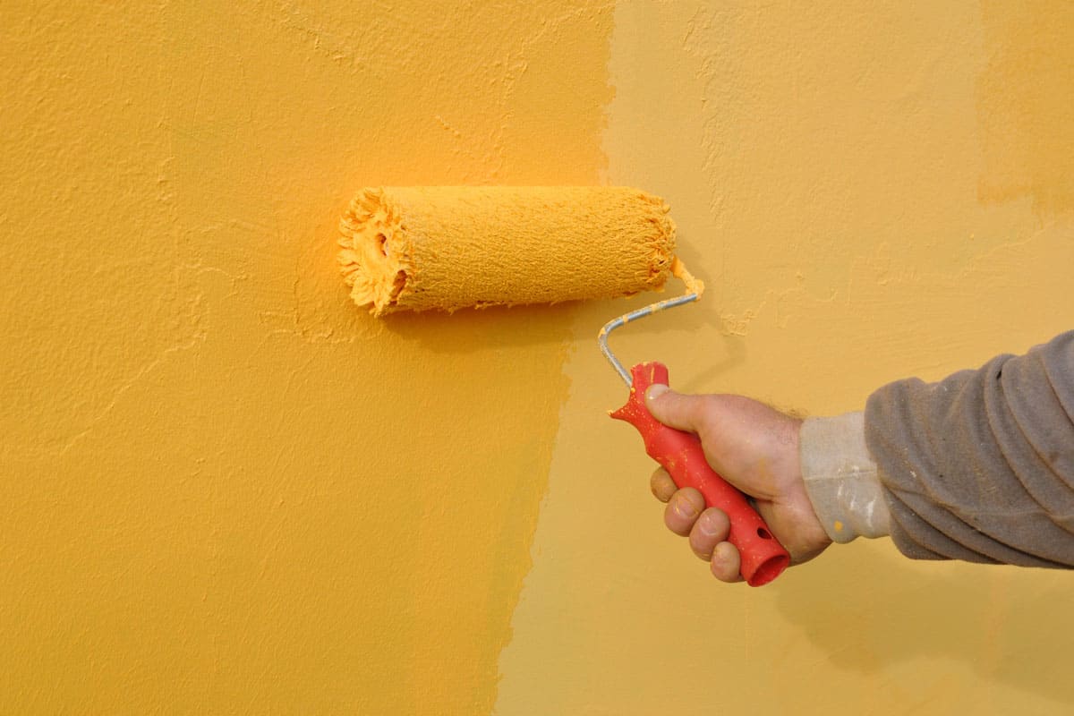 man holding roller painting the wall with yellow paint