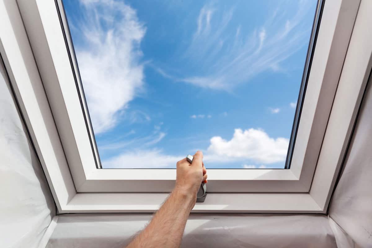 photo of man hands opening the new modern skylight mansard window on the attic