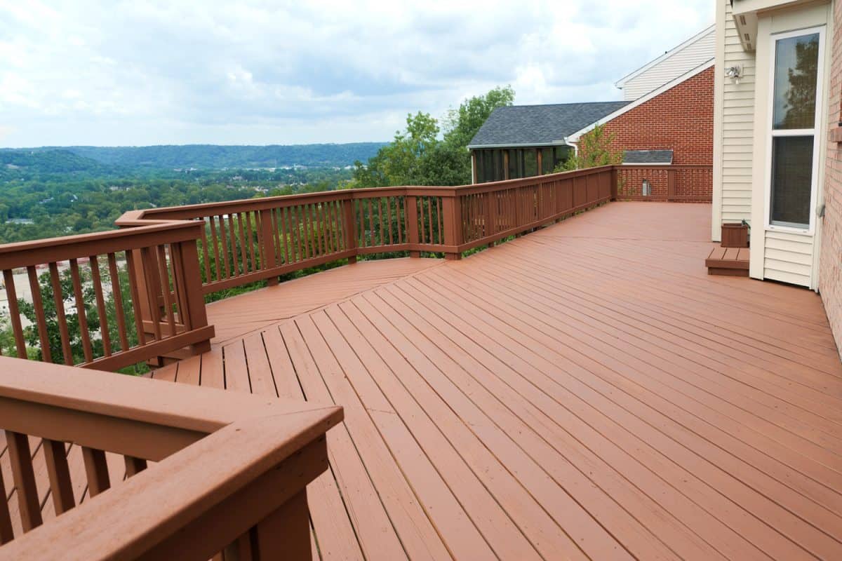 A freshly painted and stained wood deck with railing on a summer afternoon. The deck overlooks a beautiful valley and mountains in the distance.
