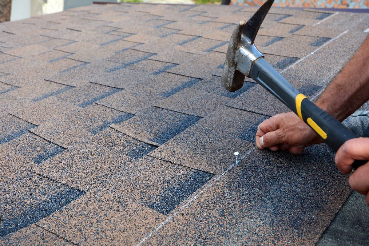 Contractor installing bitumen roof shingles with hammer and nails