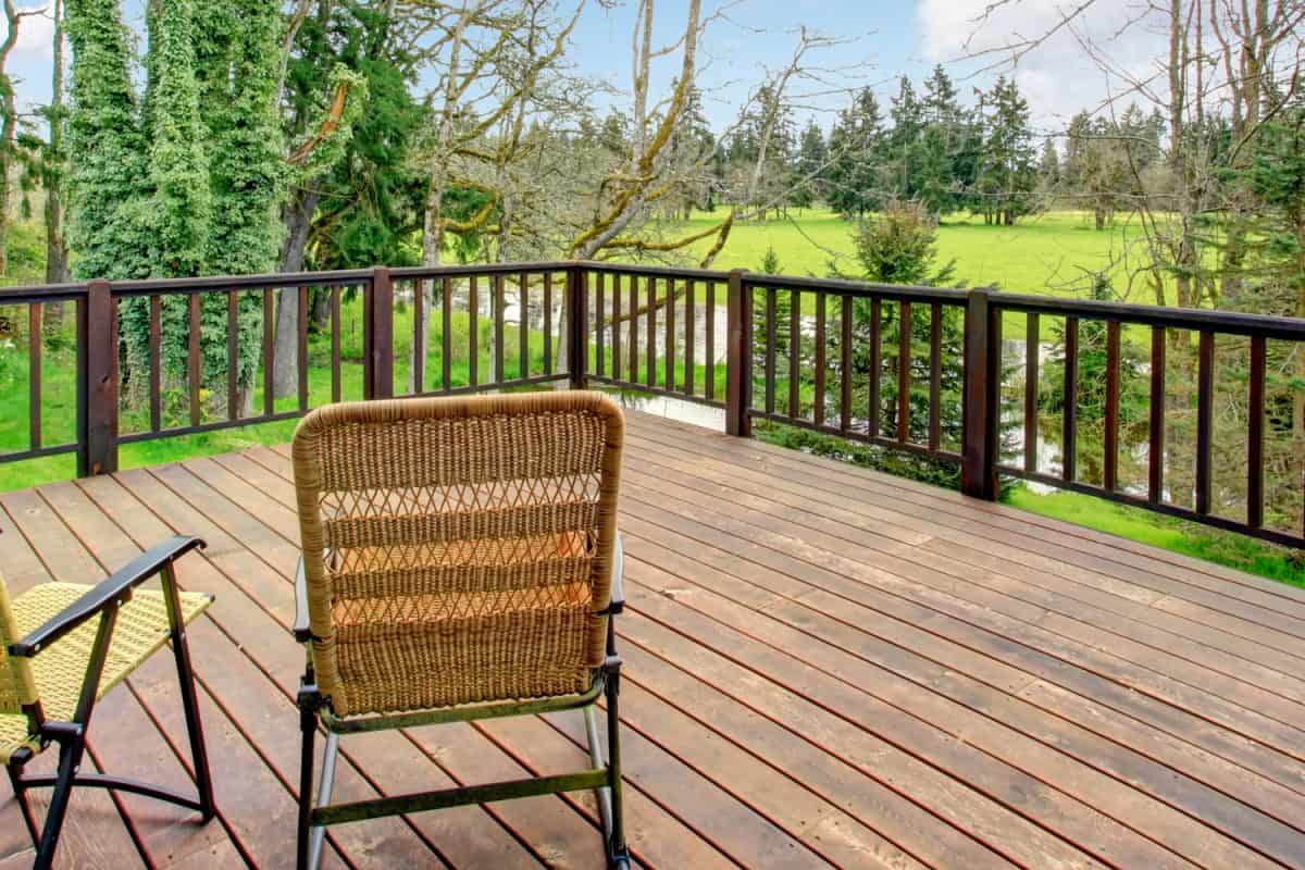 Cozy back deck with wicker chairs overlooking forest and meadow.
