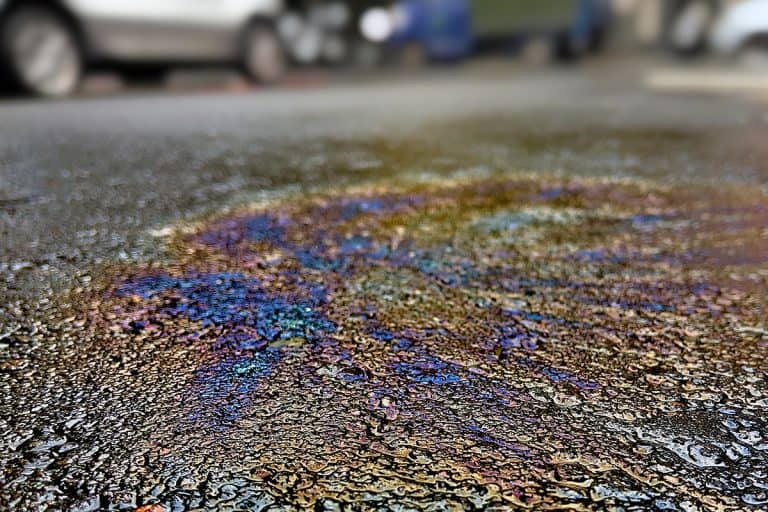 Oil spill on asphalt road with car on the background, Does Gas Stain Driveways?