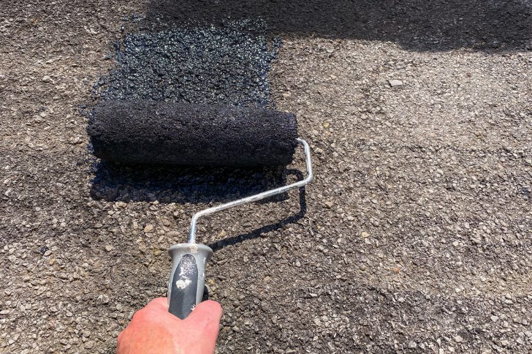 Person's hand using a roller to seal a tarmac driveway with black paint, Can Driveway Sealer Be Used On A Roof?