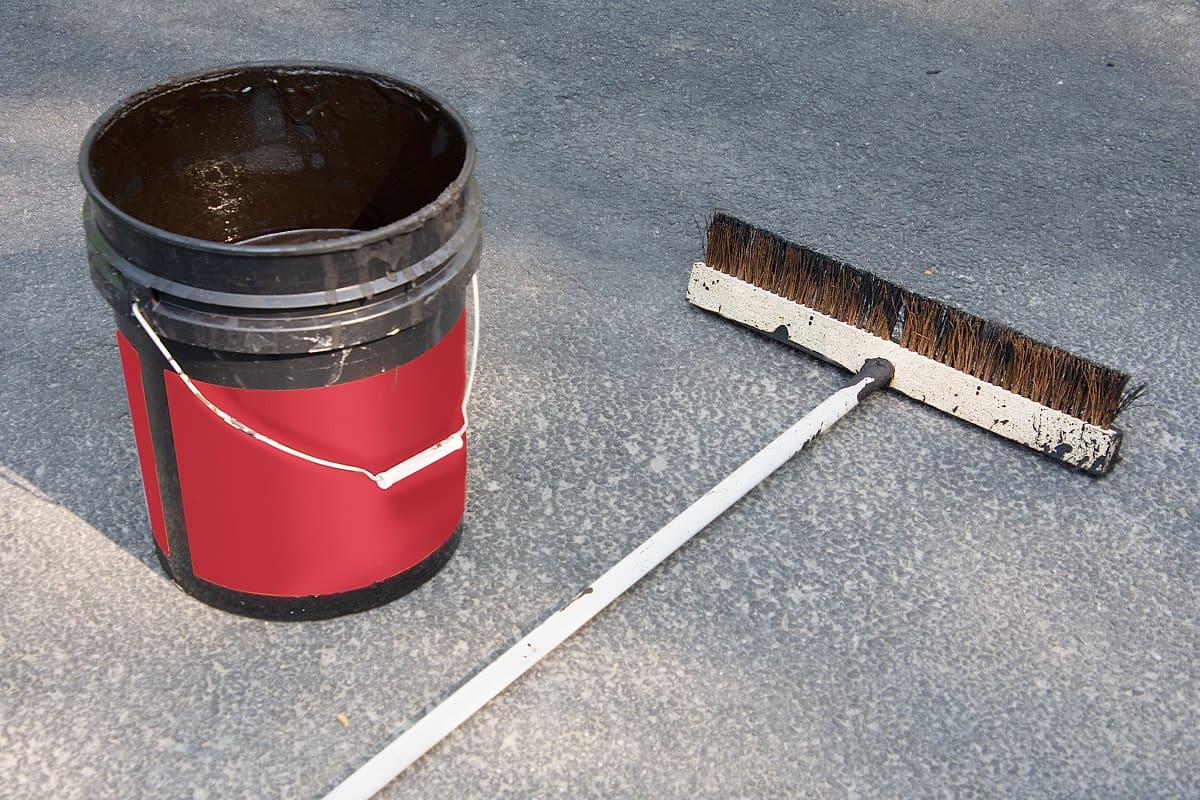 Used driveway sealing brush with bucket of asphalt sealer