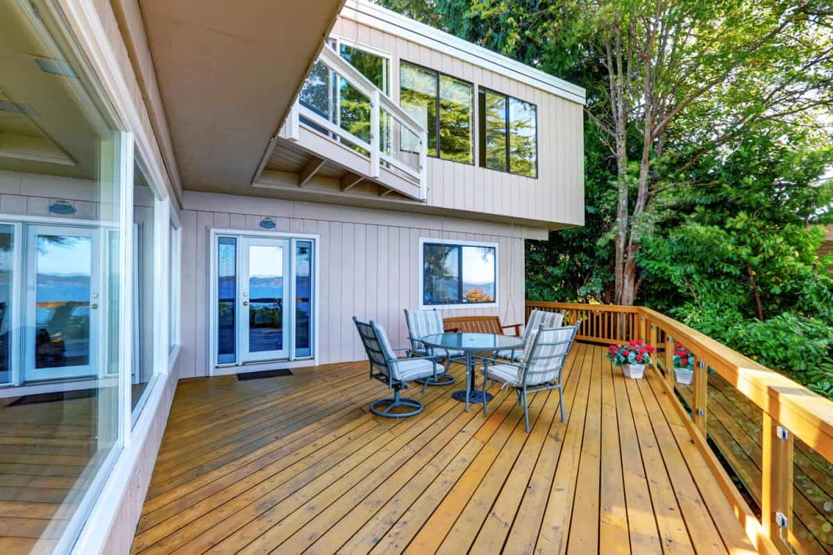 Wooden walkout deck with outdoor table set and swinging bench. Modern beige house exterior. Northwest, USA
