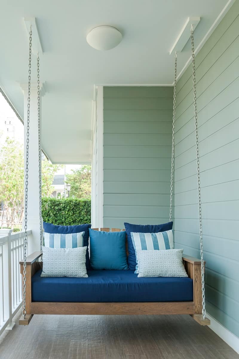How Heavy Can A Porch Swing Hold? - outdoor wooden porch swing bench with blue pillows.