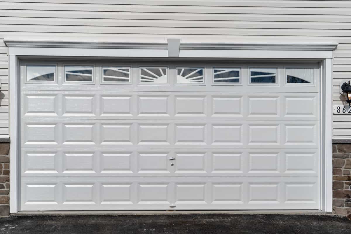 Double car classic insulated steel raised panel garage door framed with a white trim to add accent, w transom light windows divided by muntins on a new American home, 8 plain short windows decoration