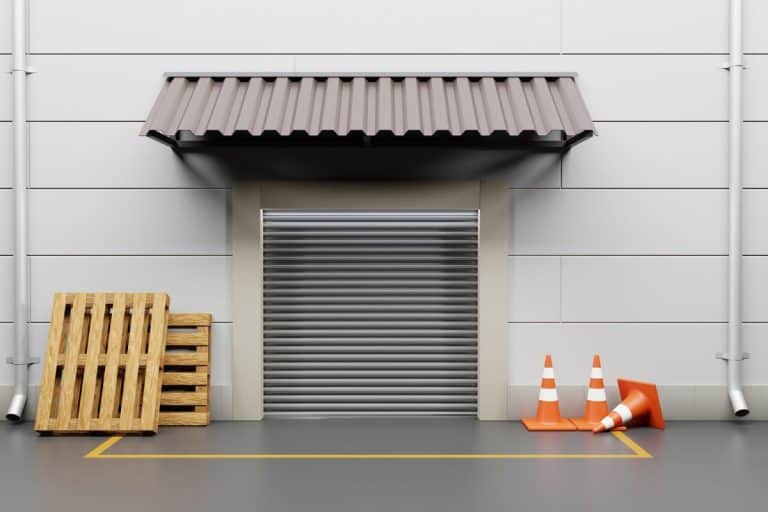 Gate warehouse with metal rolling shutter. Building front store or factory with wooden pallets and traffic cones on street. Storehouse with automatic door, yellow line road marking and awning on wall. - How To Build A Garage Door Awning