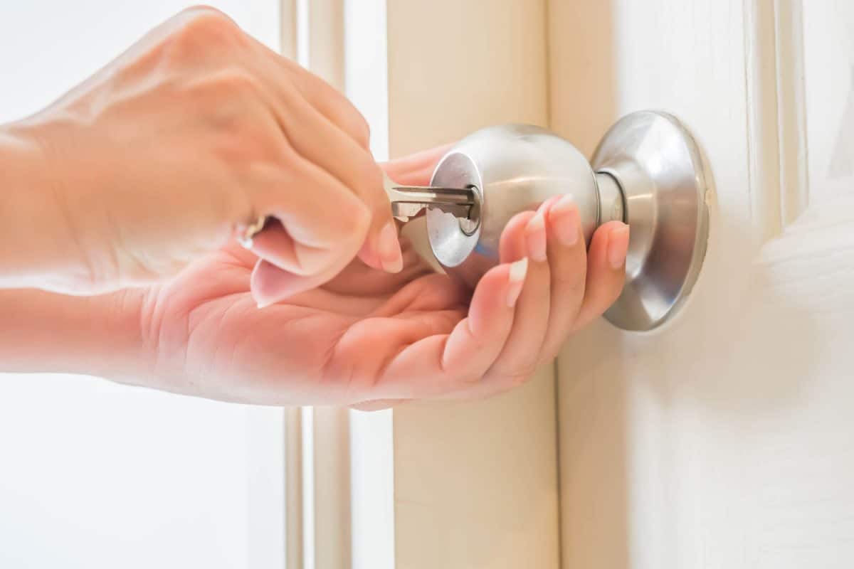 Woman with her two hands is unlocking the round door lock with the key for opening the door.

