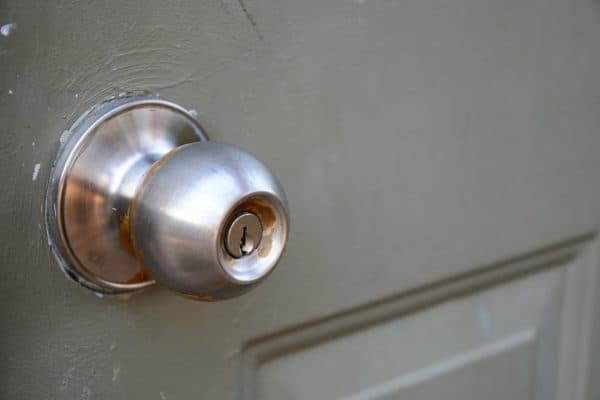 A close up image of an old and dirty metal door knob on a greyish-green painted door., Are Door Knobs Grounded?